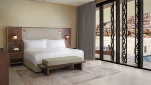 A modern bedroom with a bed, a wooden chair, and a window, lit by natural light
