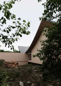 A serene building with a curved roof, surrounded by trees, featuring a combination of wood and metal materials