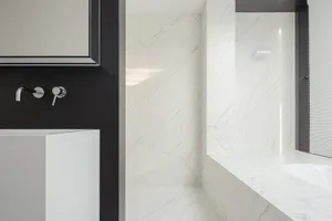Bathroom with a white sink, marble countertop, and a white bathtub against a black wall, creating a luxurious and elegant atmosphere with dim lighting