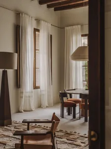 A modern dining room with a wooden dining table and chairs, a lamp, and natural light from open curtains