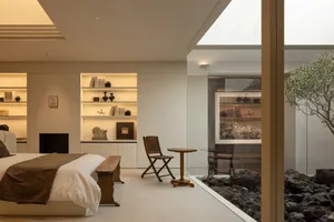 Cozy living room with a bed, chair, and table, featuring a white color scheme and natural light from a glass door