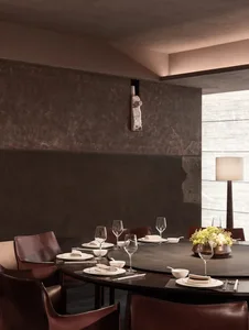 A rustic dining room with a stone wall, stone floor, and a round table set with wine glasses, plates, and cutlery, surrounded by chairs and a vase of flowers