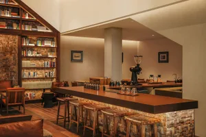 Cozy living space with a wooden floor, a wooden bar, and wooden stools, surrounded by books and a comfortable seating arrangement