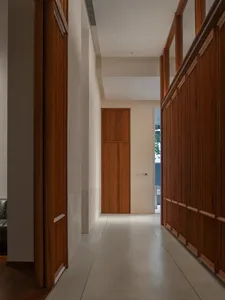 A dimly lit hallway with a wooden floor and white walls, featuring a doorway at the end