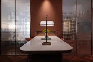 Cozy dining room with a marble table, wooden chairs, and a vase with flowers, set against a brown color scheme and dim lighting
