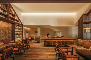 Cozy restaurant with wooden floors, high ceiling, and a mix of natural and artificial lighting, featuring multiple seating options and a warm ambiance