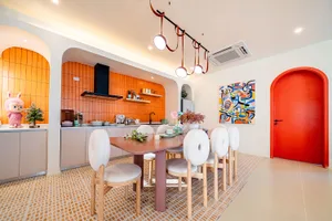 A modern kitchen and dining area with an orange refrigerator and table, a wooden dining table, and a potted plant, set in a well-lit space with a warm atmosphere