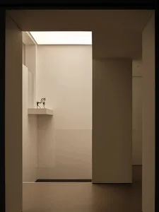 A dimly lit hallway with a white wall and floor, featuring a small statue on a shelf and a minimalist aesthetic