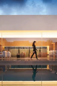A woman walks through a well-lit room with a glass wall and glass floor, featuring a couch and dining table in a comfortable and inviting atmosphere