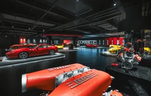 A well-lit showroom with red walls and white floors, featuring a variety of sports cars arranged in a circular fashion on a circular platform