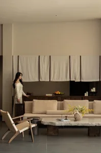 A living room with a couch, dining table, chair, and vase of flowers, featuring a mix of natural and artificial lighting and warm, inviting atmosphere