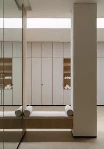 White bathroom with a large mirror, bench, and cabinet, featuring natural light and a modern design