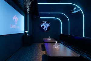 A stylish lounge or bar area with a black and blue color scheme, featuring a bar, dining table, and two couches