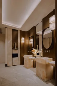 Modern bathroom with brown marble walls, a large mirror, a sink, and a toilet, with dim lighting creating a cozy atmosphere