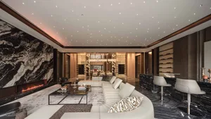 A well-lit living room with a white couch, chair, dining table, and books, featuring a clean and modern aesthetic