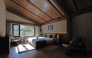 Cozy bedroom with a bed, chair, and window, featuring a wooden floor and ceiling, and well-lit with a bright atmosphere