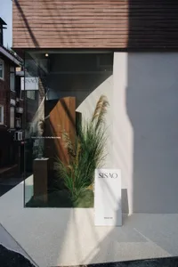 A storefront with a display of plants and a sign, featuring a glass door and window, with natural light and a modern appearance