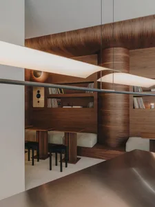 A dimly lit room with wooden walls and floors, featuring a dining table, bookshelf, and couch, creating a warm and cozy atmosphere