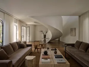 Comfortable and inviting living space with a large couch, coffee table, and spiral staircase, surrounded by natural light and decorative elements