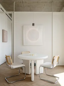 A modern dining area with a white table and four wooden chairs, set in a well-lit room with a clean and minimalistic design