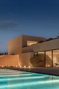 A modern house with a concrete exterior, a swimming pool, and a large rock in the living room, set in a dimly lit atmosphere