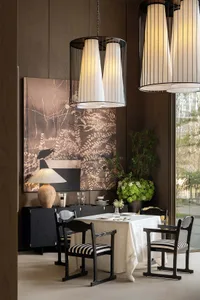 Dining room with a table set for a meal, surrounded by chairs, wine glasses, and vases, with a large painting on the wall in a well-lit, modern space