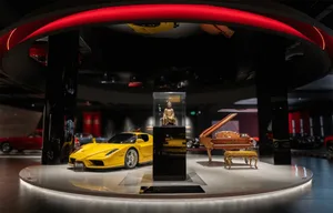 A modern showroom featuring a variety of vehicles and a piano, with a red hue and upscale ambiance