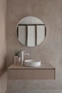 A modern bathroom with a white sink, large round mirror, and marble countertop, set against a wooden vanity, in a well-lit space