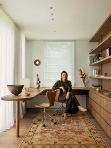A woman sits in a chair in a cozy home office with a desk and bookshelf, surrounded by natural and artificial lighting