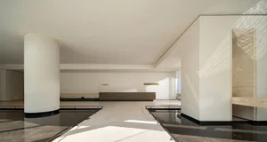 A large, empty modern lobby with a white ceiling and walls, a tile floor, and natural light from windows