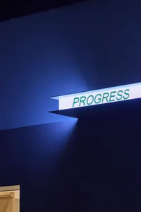 A blue-lit sign reading Progress mounted on a wall, giving a futuristic appearance