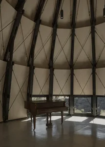 A dimly lit room with a dome-shaped ceiling, featuring a wooden floor and a piano as the central focal point, surrounded by a wooden structure