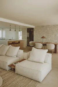 Cozy modern living room with a large couch, dining table, and kitchen area, decorated with books and a vase, under dim lighting