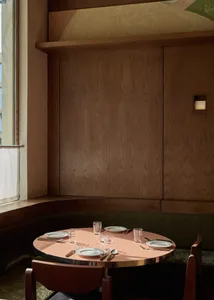 A dining room with a wooden table and chairs, set with plates, glasses, and cutlery, surrounded by a warm and inviting atmosphere with natural light from a window