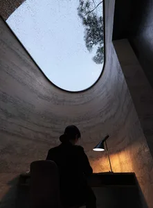 A person sits at a wooden desk in a study with a window providing natural light, surrounded by drywall and neutral colors
