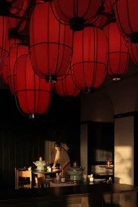 A woman stands near a dining table with red lanterns hanging from the ceiling in a cozy restaurant setting with a warm ambiance