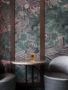 A modern dining space with a table, chairs, and a mural of waves on the wall, with a beer on the table and natural light creating a relaxed atmosphere