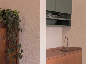A small kitchen with a white wall, green cabinet, and a metal sink on the right, accompanied by a green potted plant on the left, creating a cozy and inviting atmosphere