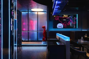 A modern restaurant with a blue and red color scheme, featuring a red robot statue and neon sign, comfortable seating, and dim lighting