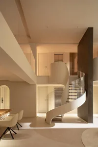 A modern building with a white marble spiral staircase surrounded by a glass wall, flooded with natural light and featuring a couch for relaxation