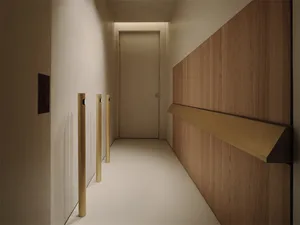 A calm and inviting hallway with a wooden floor and white walls, featuring a doorway and a wall-mounted light