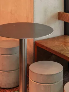 A modern dining room with a round wooden table and metal base, three chairs, and a bench, well-lit with natural light from a window