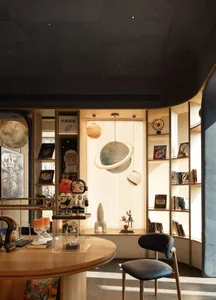 A modern room with a wooden table and chair, blue color scheme, and a large window, featuring a collection of books, a clock, and space-themed figurines