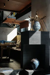 A well-lit living room with a black couch, a dining table, and a decorative vase, creating a comfortable and inviting atmosphere