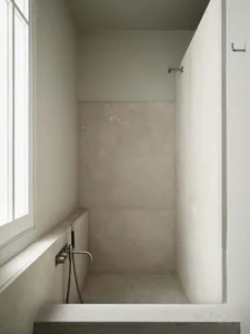 A clean bathroom with a white concrete shower stall and a window, well-maintained and minimalist