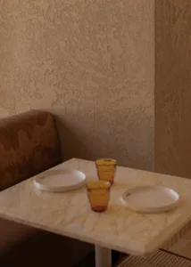 Dining room with a table and chairs, set with plates and glasses, surrounded by a cozy and inviting space with a patterned wall and soft warm lighting