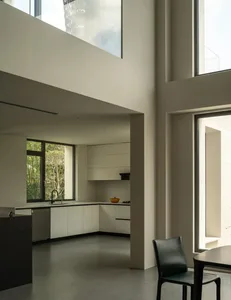 A modern kitchen and dining area with white walls, a dining table, chairs, a couch, and a chair, well-lit by natural light through windows