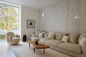 Cozy modern living space with a large couch, coffee table, and potted plants, featuring wood and fabric materials and natural light from a window