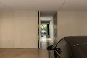 A calm and inviting living room with a white color scheme, natural light, and a doorway leading to a hallway and garage