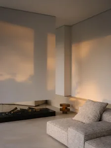 A modern living room with a couch in front of a fireplace, a glass door, and a white wall, lit by natural sunlight